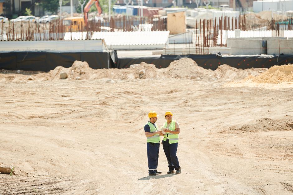 Doi muncitori discutând planuri pe un șantier de construcții